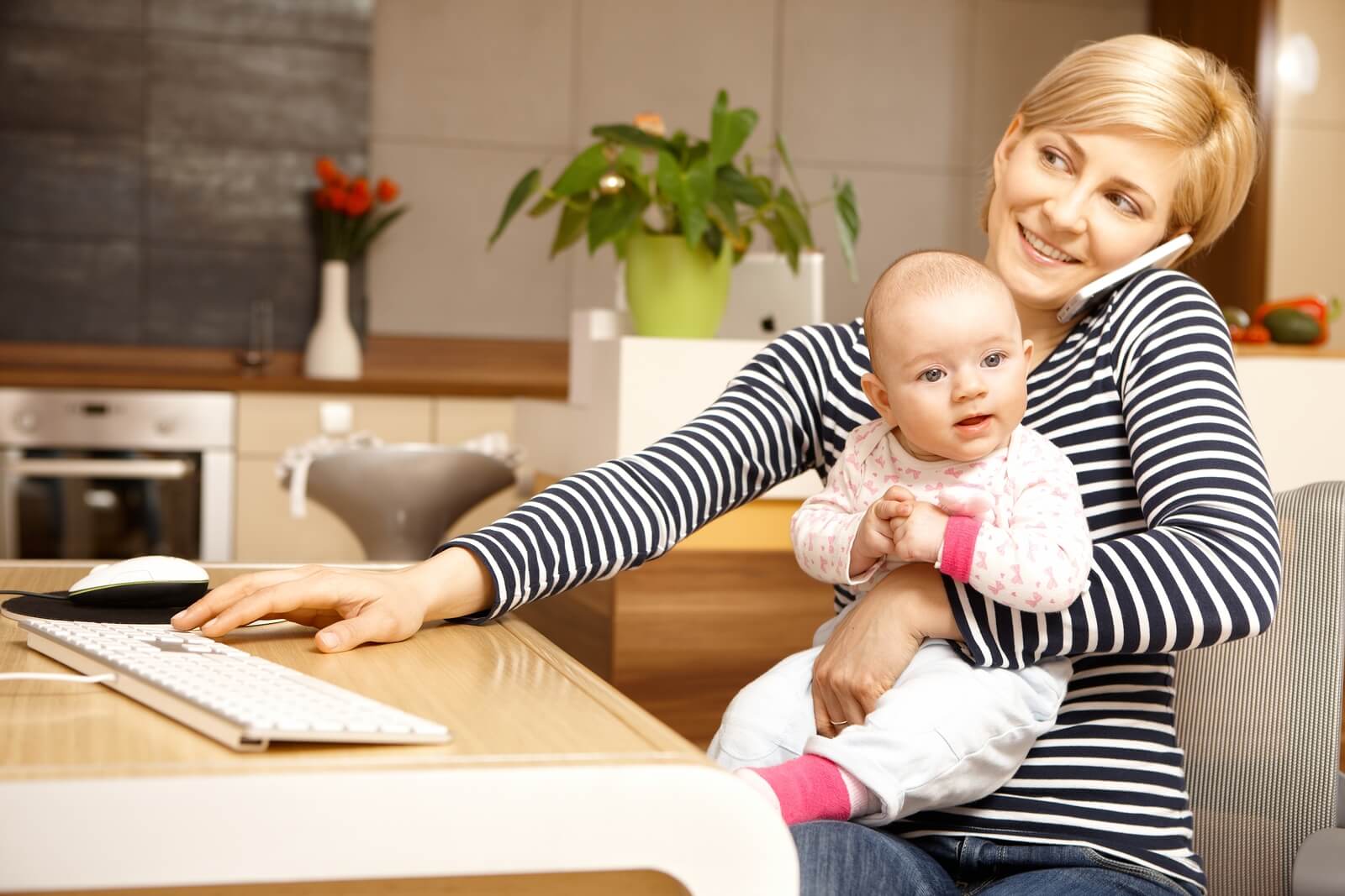 Businesswoman working from home, holding baby girl on lap.